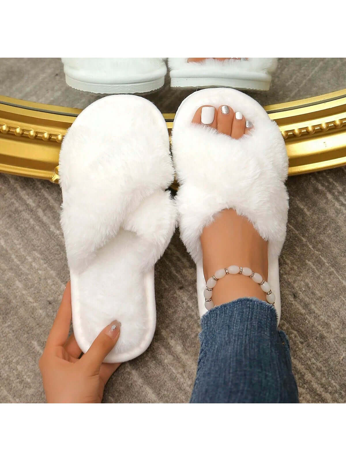 Close-up of white Axon Cloud-Soft cross strap fur slippers worn with denim jeans and a stylish anklet.